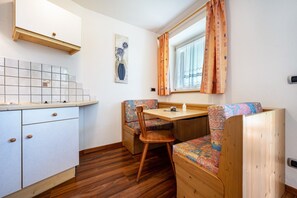 Une petite cuisine fonctionnelle avec un plan de travail carrelé, une table à manger en bois et un banc agrémenté d’un coussin à motifs.