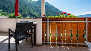 A balcony with a wicker chair, a red umbrella, and a wooden fence with decorative glass panels. - Studio Apartment "Talblick 2" with Mountain View, Garden and Wi-Fi (Lajen)