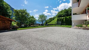 A gravel driveway leading to a building with a wooden facade and a white building with balconies. - Studio Apartment "Talblick 2" with Mountain View, Garden and Wi-Fi (Lajen)