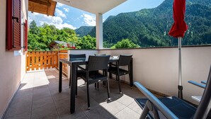 A balcony with a table and chairs, a red umbrella, and a view of a forested mountain. - Holiday Apartment "Talblick 3" with Mountain View, Garden and Wi-Fi (Lajen)