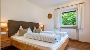 A wooden bed with white bedding, a nightstand, a bedside lamp, a window with curtains, and a wooden headboard. - Holiday Apartment "Talblick 3" with Mountain View, Garden and Wi-Fi (Lajen)