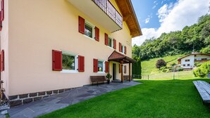 Ein zweistöckiges Gebäude mit steinernen Fundament, roten Fensterläden und einer Veranda.
