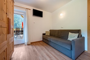 Une pièce avec un canapé gris, un téléviseur à écran plat fixé au mur et une armoire en bois.