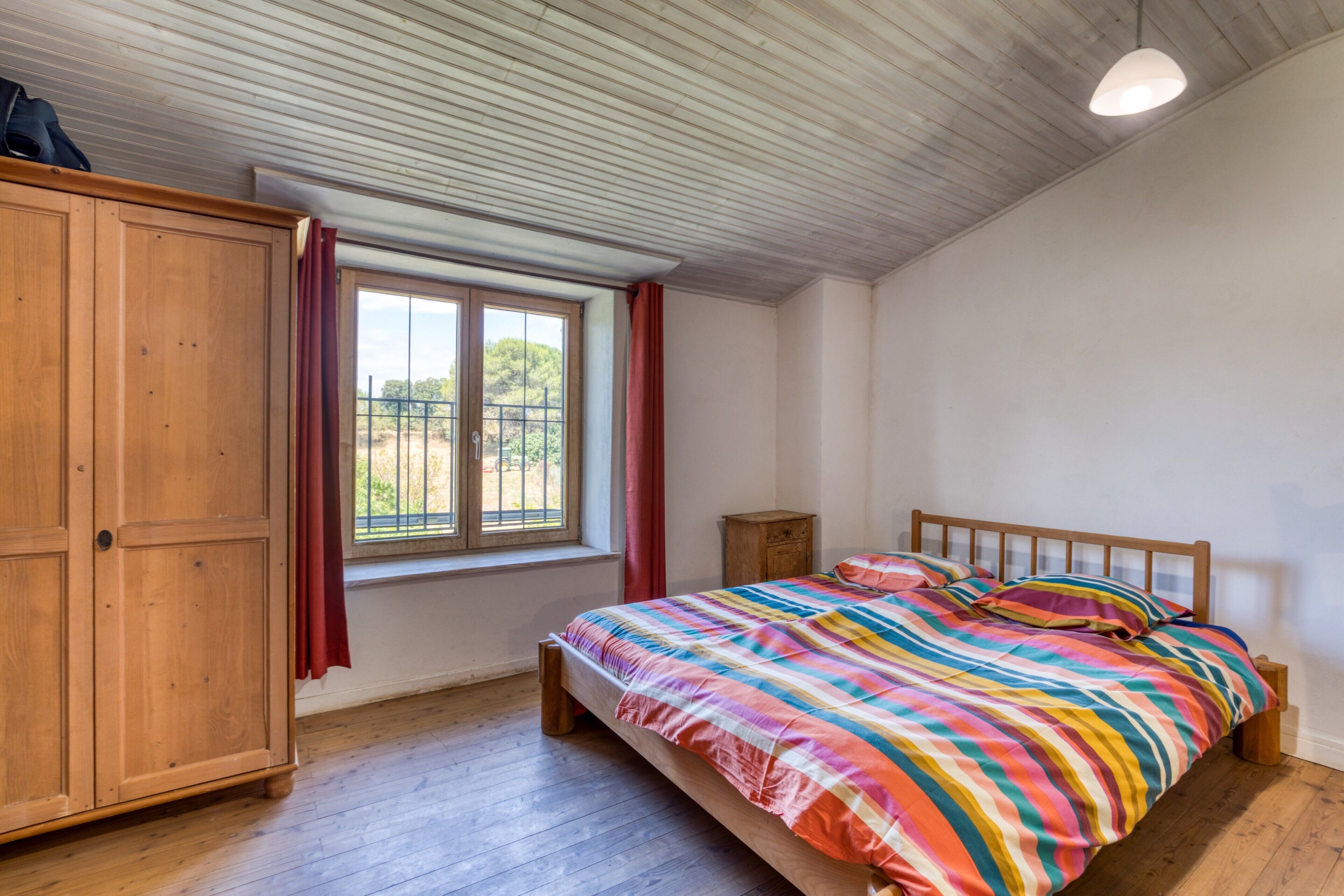 Une chambre à coucher avec un lit en bois, une armoire, une fenêtre avec des rideaux et un luminaire au plafond.