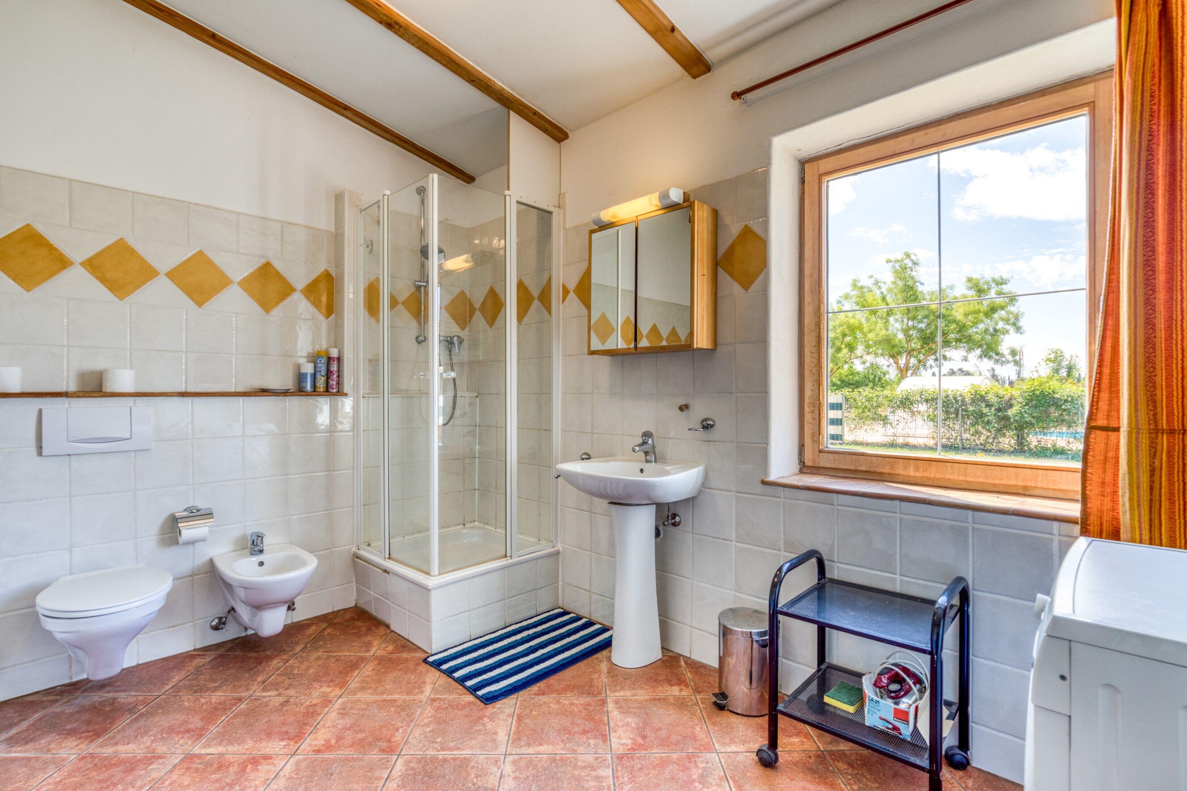A bathroom with a shower, toilet, bidet, sink, and a window with a view.