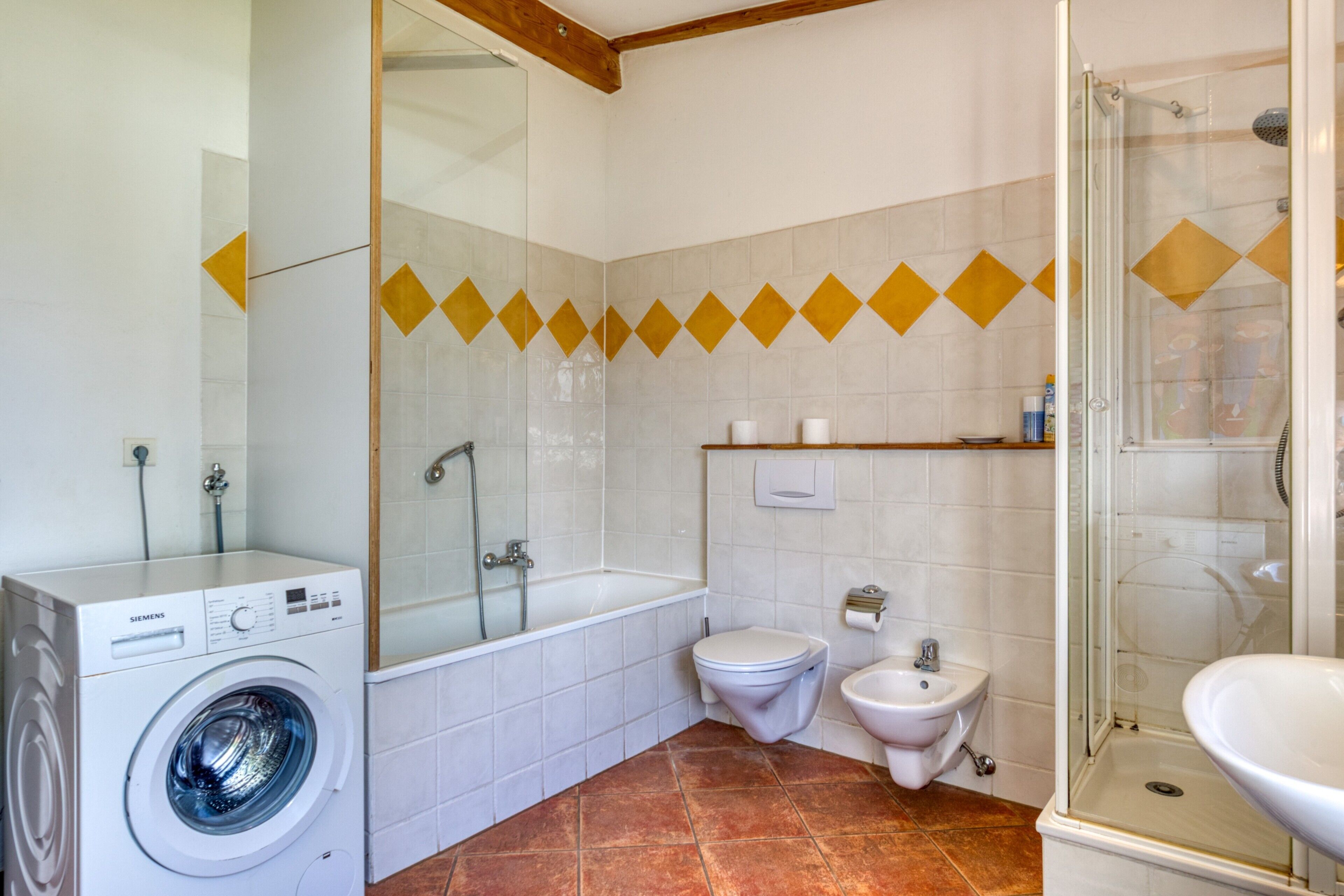 Un baño con lavadora, bañera, inodoro, bidé y ducha con mampara de vidrio.