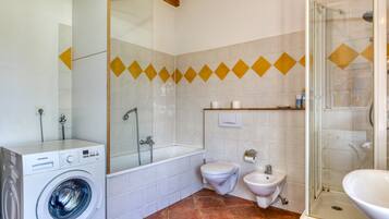 Un baño con lavadora, bañera, inodoro, bidé y ducha con mampara de vidrio.
