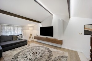 A modern living room with a sofa, a TV on a wooden wall unit, a patterned rug, and a floor lamp. - Holiday Apartment 'Dolce Soggiorno - Soldano' with Sea View, Terrace & Wi-Fi (Soldano)