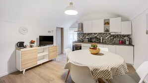 A compact kitchen with a dining area, a television, and a clock on the wall.