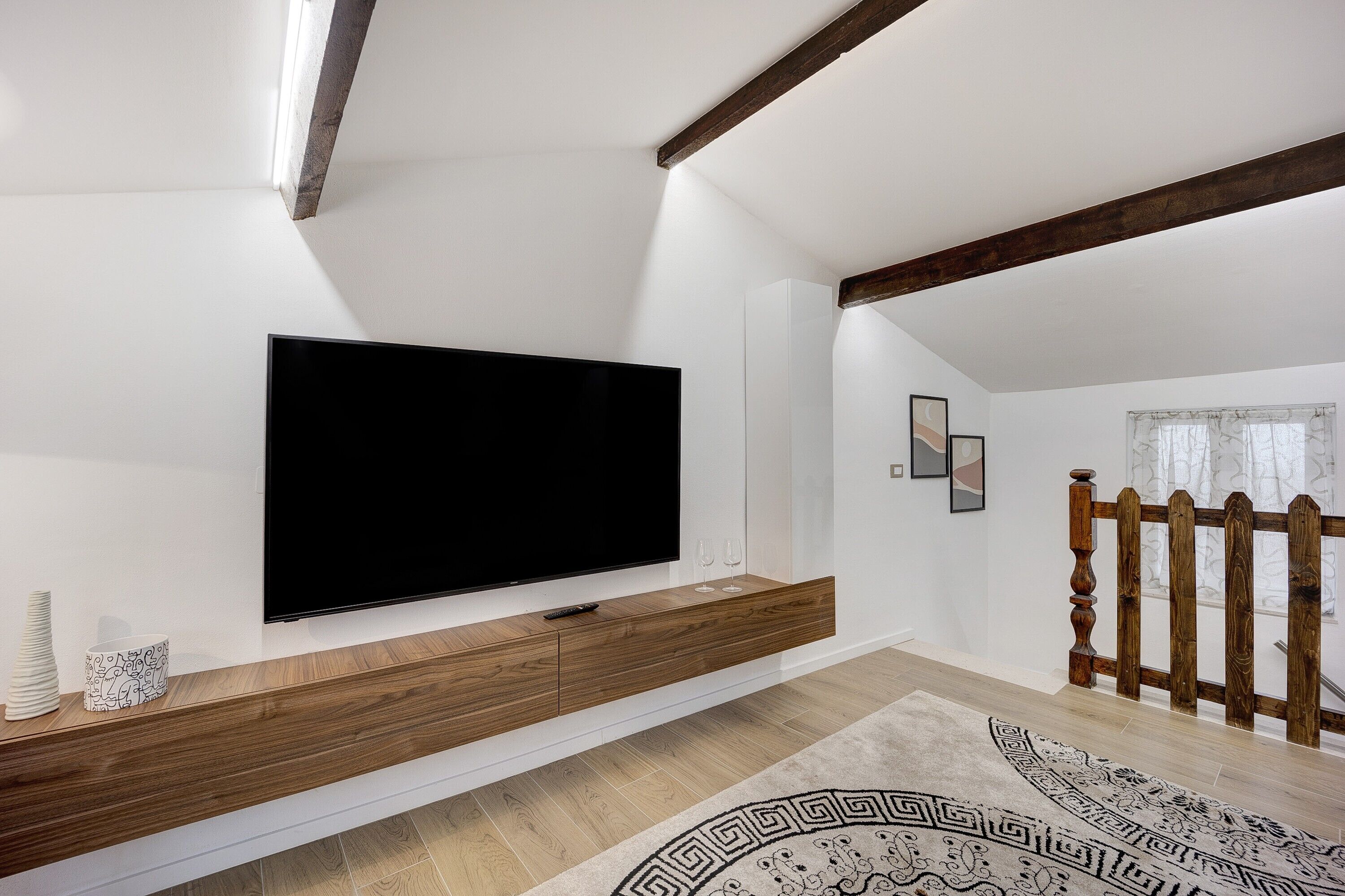 Ein modernes Wohnzimmer mit einem an einer Holzkonsole montierten Flachbildfernseher, einem gemusterten Teppich und einer Holztreppengeländer.