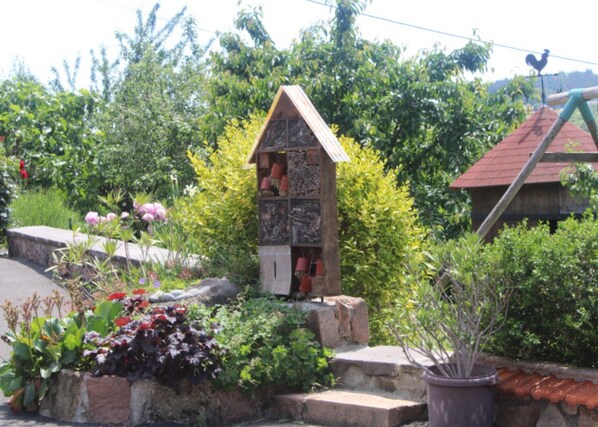 Una pequeña estructura de piedra con techo triangular, rodeada de abundante vegetación y diversas plantas.