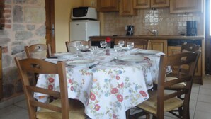 Une table à manger dressée pour quatre personnes, avec des nappes à motifs floraux, des chaises en bois et un mur en pierre.