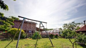 Un jardin avec une balançoire, un bâtiment en briques et une serre.
