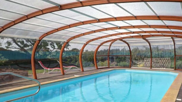 Une piscine couverte avec un toit en verre, entourée d’une structure en bois.