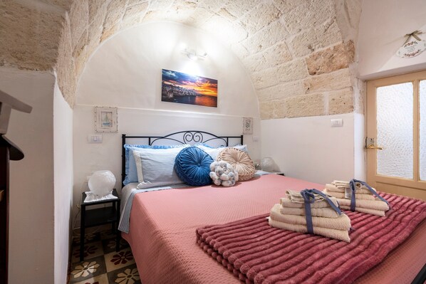 A bedroom with a stone ceiling, a bed with a pink bedspread, and a painting of a sunset.