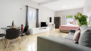 Una habitación de hotel moderna con comedor, sofá, televisor, cama y ventana con vista a la calle.