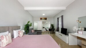 Un dormitorio moderno con una cama, un escritorio, un televisor y un rincón de comedor al fondo.