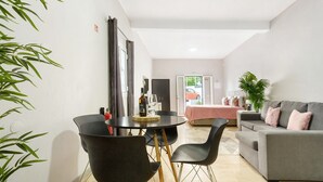 Una sala moderna con un sofá gris, sillas negras, una mesa de comedor con una botella y una planta.