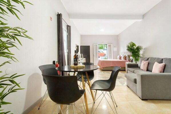 A modern living room with a grey sofa, black chairs, a dining table with a bottle, and a plant.