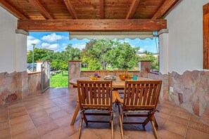 Eine Terrasse im Freien mit Holztisch und -stühlen, Steinmauern und Blick auf Grünflächen und Gebäude.