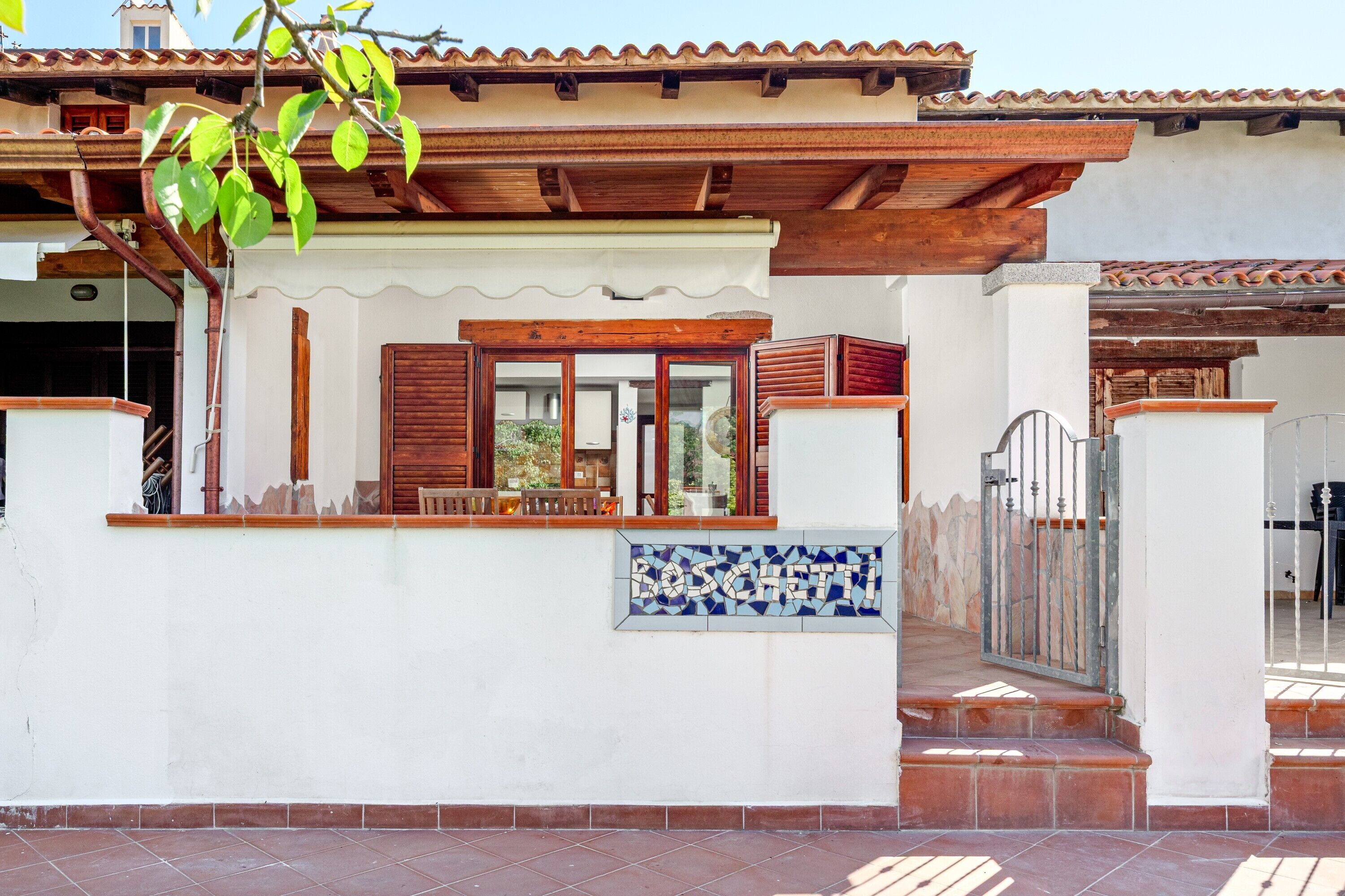 A building with a tiled entrance, a wooden balcony, and a tiled wall with a name.