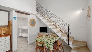A compact room with a dining table, chairs, a TV, a bunk bed, and a staircase.