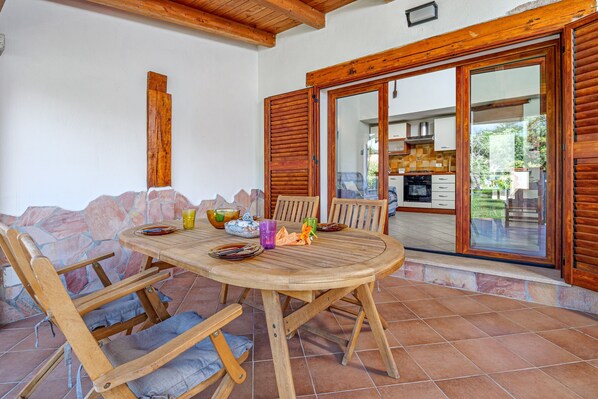 A wooden dining table with chairs, a stone wall, and a view into a kitchen and dining area.