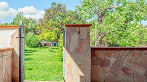 A stone wall with a tiled floor, a metal gate, and a grassy area with trees in the background.