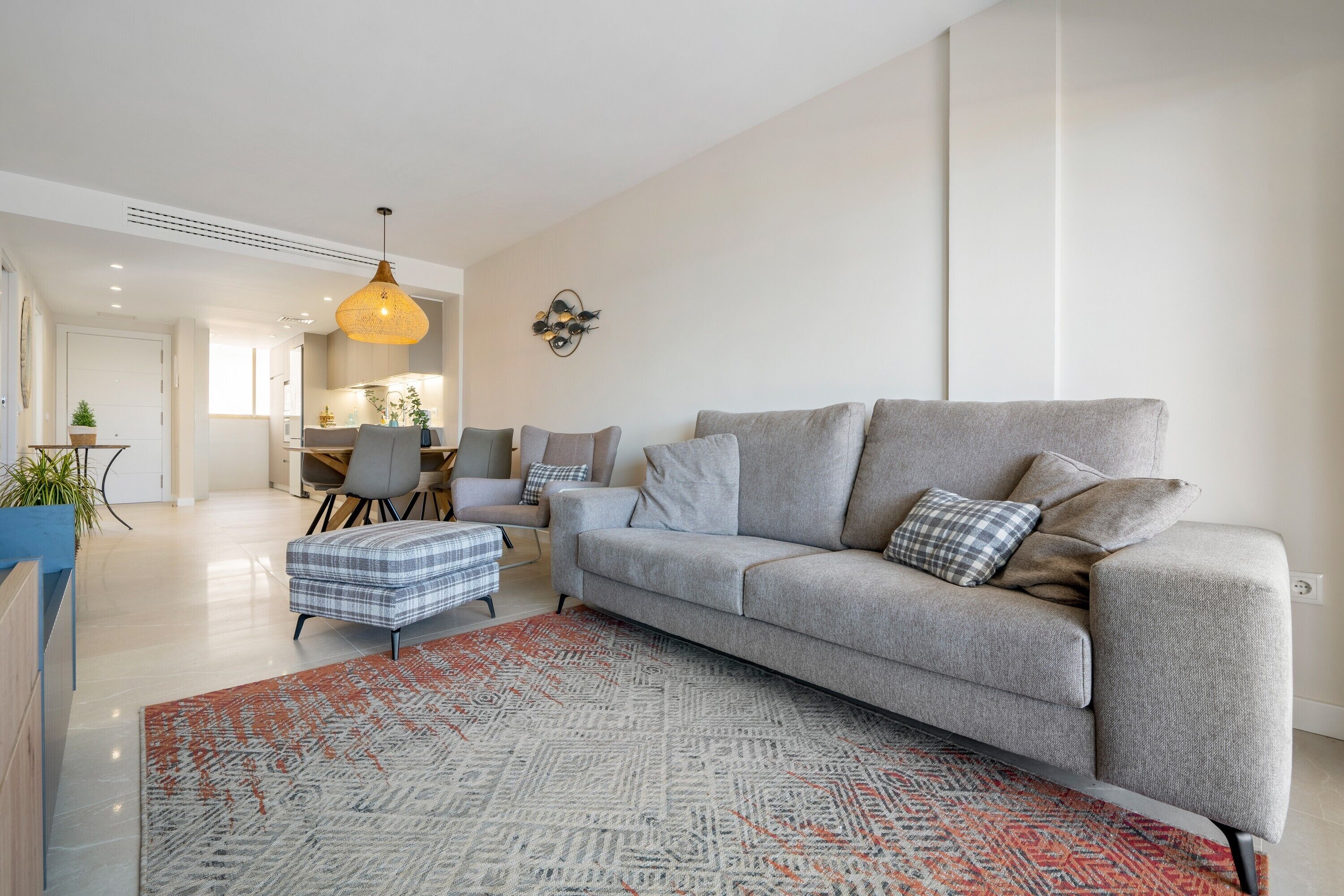 A modern living room with a grey sofa, ottoman, and patterned rug.