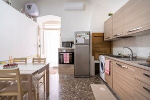 A compact kitchen with a microwave, refrigerator, oven, and washing machine. - Holiday Apartment "Chiarina Rooms" with A/C & Wi-Fi (Polignano a mare)