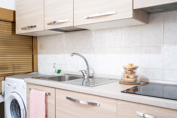 Una cocina moderna con un lavamanos de acero inoxidable, armarios de madera, lavadora integrada y un tarro de vidrio sobre la encimera.