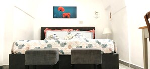 A bed with a patterned bedspread, two pillows, and a headboard. There is a chair to the right of the bed and a lamp on the wall. - Holiday Apartment "Chiarina Rooms" with A/C & Wi-Fi (Polignano a mare)