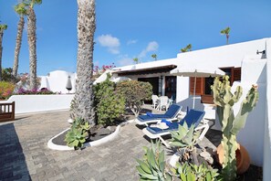 Une terrasse avec des chaises longues, un cactus et un bâtiment blanc doté d’un toit recouvert de tuiles.