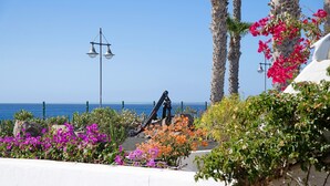 Un jardín costero con un muro blanco, una escultura de metal y un farol.