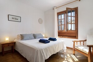 Une chambre à coucher avec un lit, des tables de chevet, une chaise, une fenêtre avec des rideaux et une horloge murale.