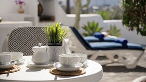 Una terraza soleada con una mesa preparada para el té, sillones de descanso y plantas en macetas.