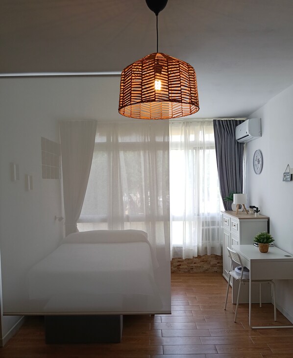 A bedroom with a bed, a desk, a chair, a hanging light fixture, and a window with curtains. - Studio Apartment 'Torremolinos' with Shared Pool, Shared Garden & Wi-Fi (Málaga)