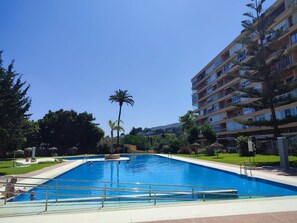 A swimming pool with a clear blue water surface, surrounded by a tiled deck and a grassy area with trees.