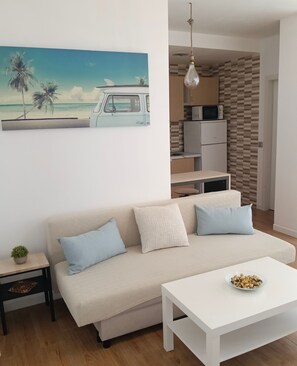 A modern living room with a sofa, a coffee table, and a painting of a beach scene. - Studio Apartment 'Torremolinos' with Shared Pool, Shared Garden & Wi-Fi (Málaga)
