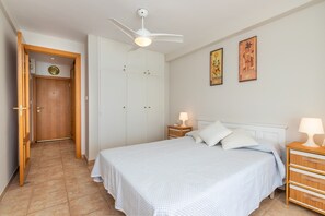 A bedroom with a bed, nightstands, a ceiling fan, a wardrobe, and artwork on the wall.