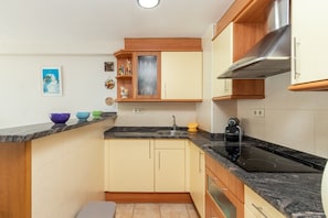 Een kleine keuken met een spoelbak, fornuis en houten keukenkastjes.