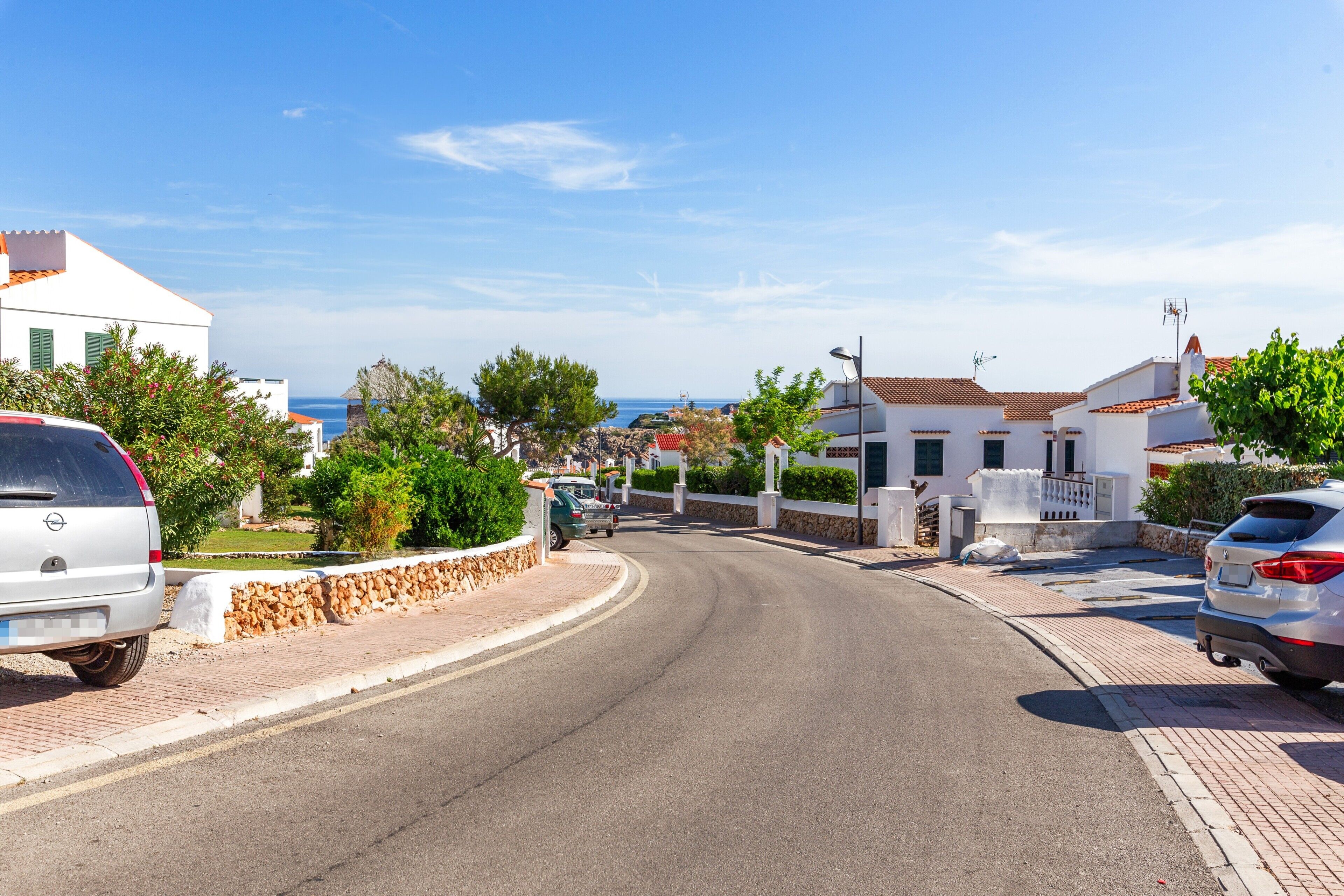 Una calle residencial con casas, coches aparcados y una vista despejada del mar.