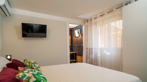 Un dormitorio con cama, televisión en la pared y ventana con cortinas.