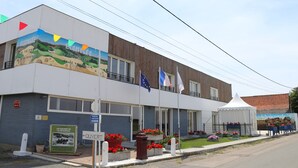 A building with a mural, flags, and outdoor flower beds. - Apartment 'Les Racines De La Vie Rurale' with Wi-Fi and Air Conditioning (LEDRINGHEM)