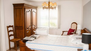A bedroom with a wooden bed, a wooden wardrobe, a chair, a bedside table, a lamp, and a window with blinds. - Apartment 'Les Racines De La Vie Rurale' with Wi-Fi and Air Conditioning (LEDRINGHEM)