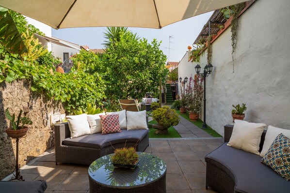 An outdoor patio with wicker furniture, potted plants, and a pergola providing shade.