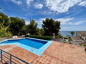 A rectangular swimming pool with a tiled deck, surrounded by trees and overlooking a body of water.
