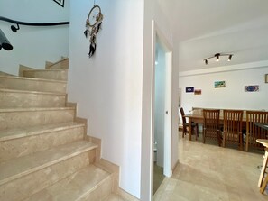 A staircase leading to a dining area with a table and chairs, a dreamcatcher on the wall, and a ceiling light fixture.
