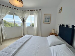 A bedroom with a bed, a nightstand, a lamp, a window with curtains, and a framed picture on the wall.