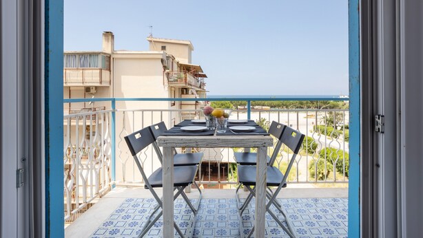 Un balcón con una mesa dispuesta para dos, barandilla y vista al mar.